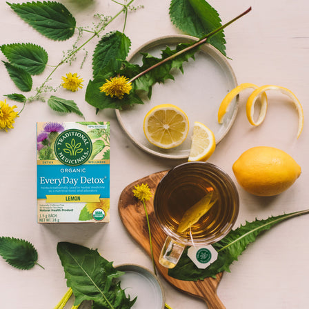 EveryDay Detox® Lemon Tea box with added lemon slices, dandelion leaves, and a cup of tea on a light background promotes healthy liver and kidney function.